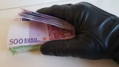 Ruka v čiernej rukavici drží balík 500 eurových bankoviek
